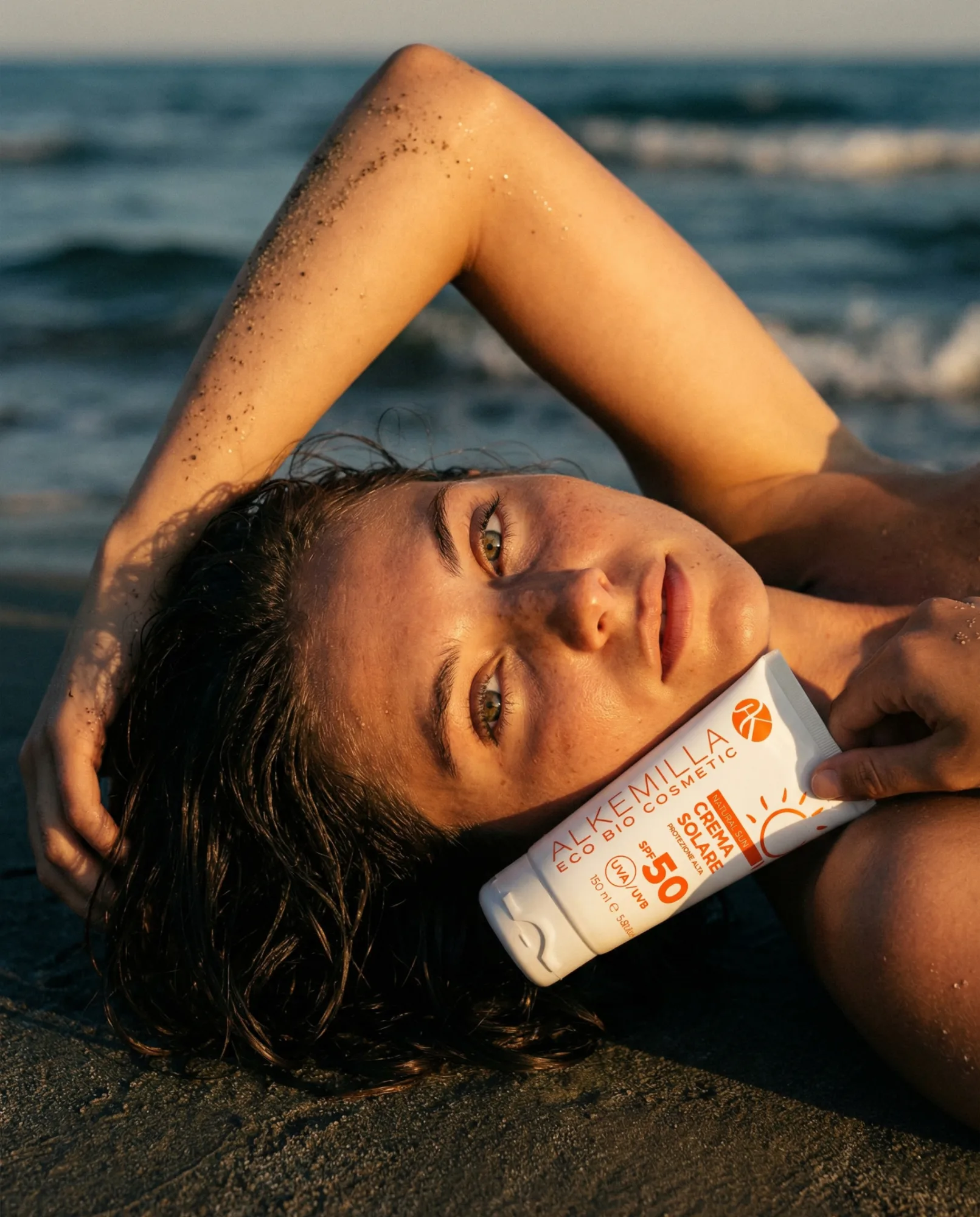 Modella distesa sulla spiaggia al tramonto con crema solare SPF 50, fotografia beauty lifestyle in ambiente marino