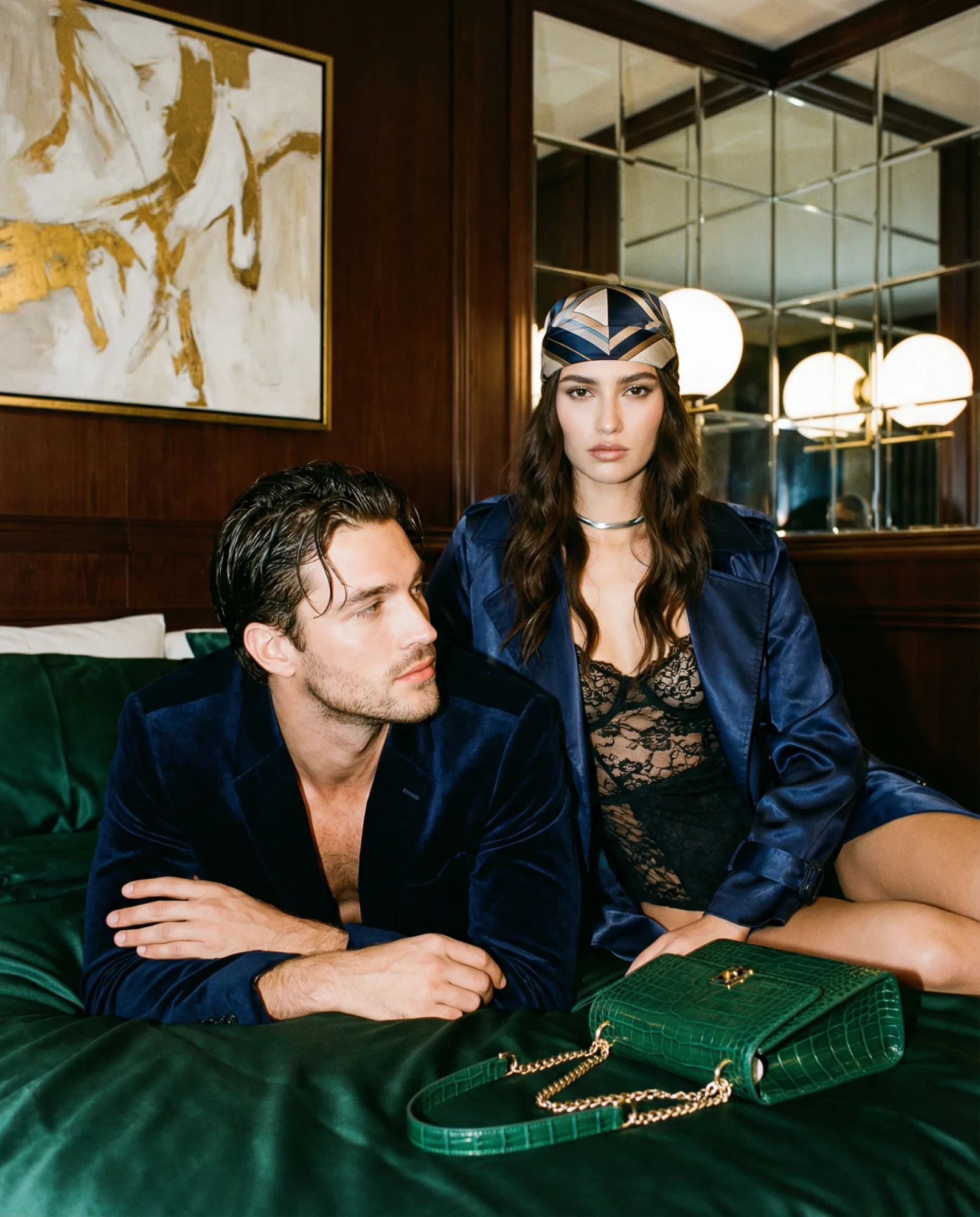 Coppia elegante seduta su un letto in una stanza d’hotel con arredamento sofisticato.  EN: