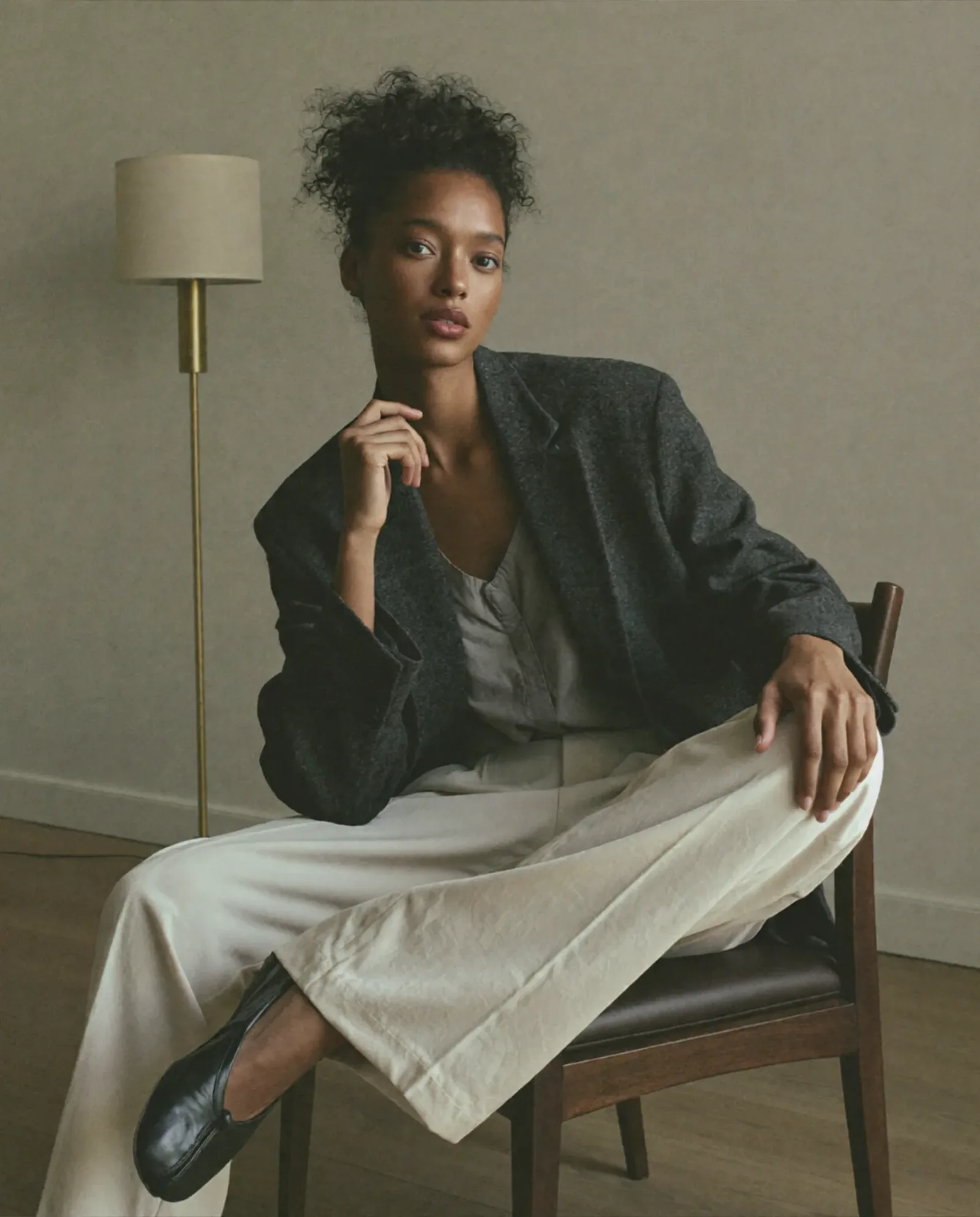 Donna seduta su una sedia in un interno minimalista con abito elegante e blazer.