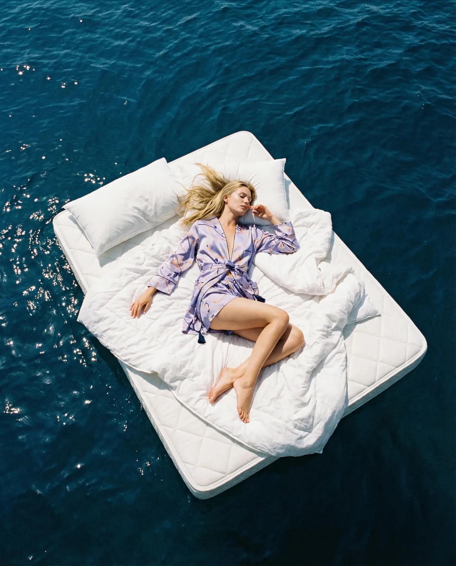 Donna sdraiata su un materasso che galleggia in mare aperto vista dall’alto.