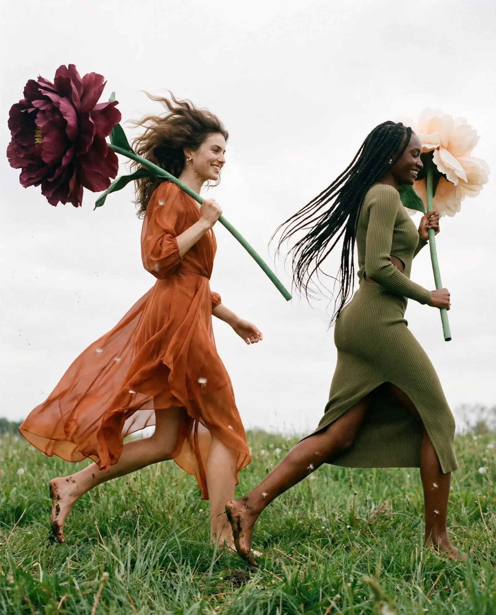Due donne che corrono in un prato indossando abiti colorati mentre tengono grandi fiori.