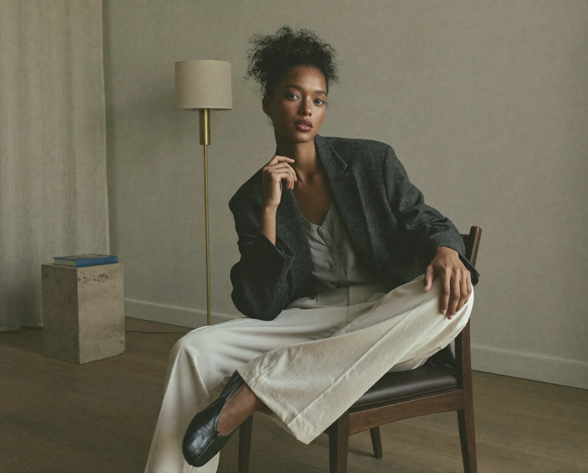 Donna seduta su una sedia in un interno minimalista con abito elegante e blazer.