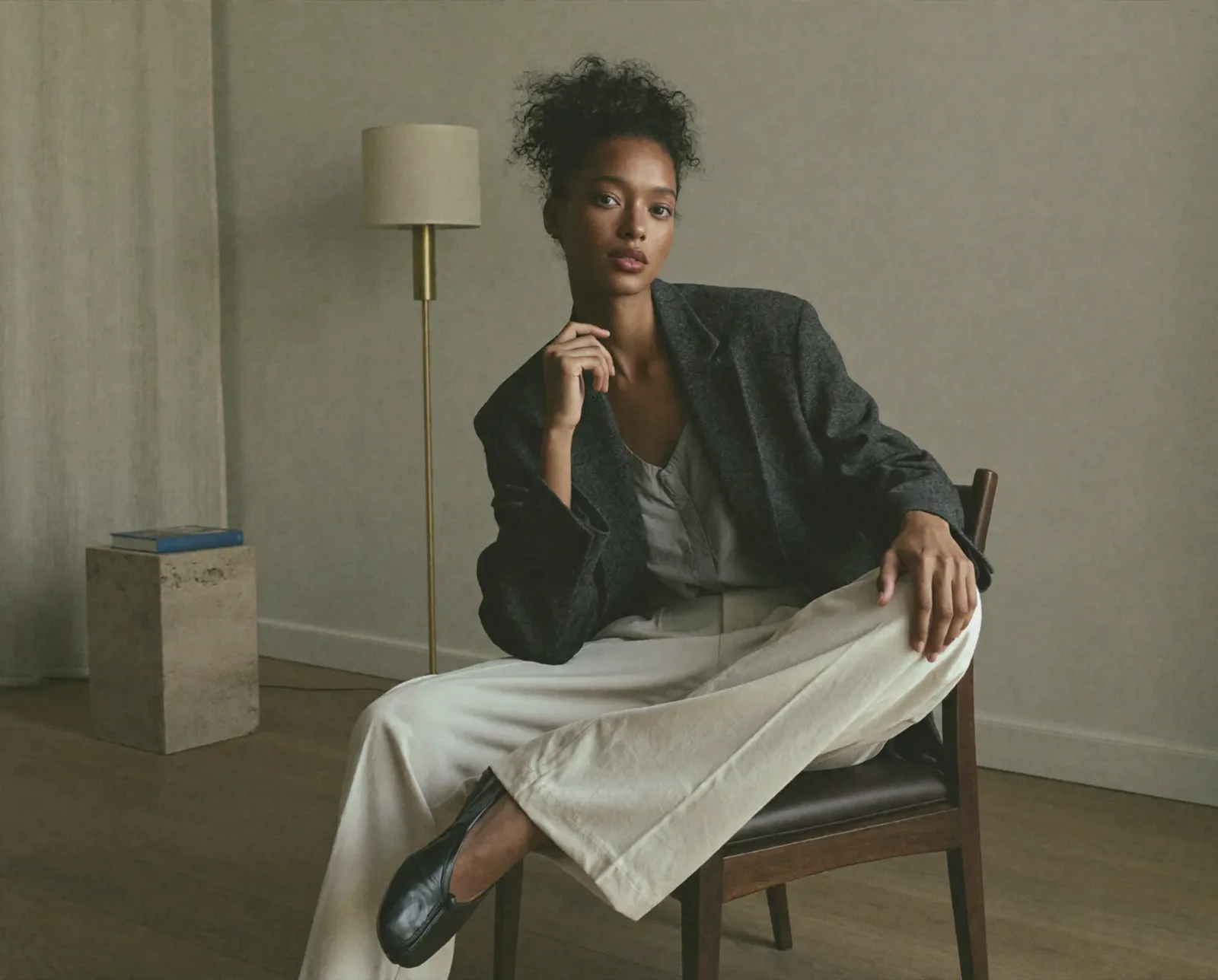 Donna seduta su una sedia in un interno minimalista con abito elegante e blazer.