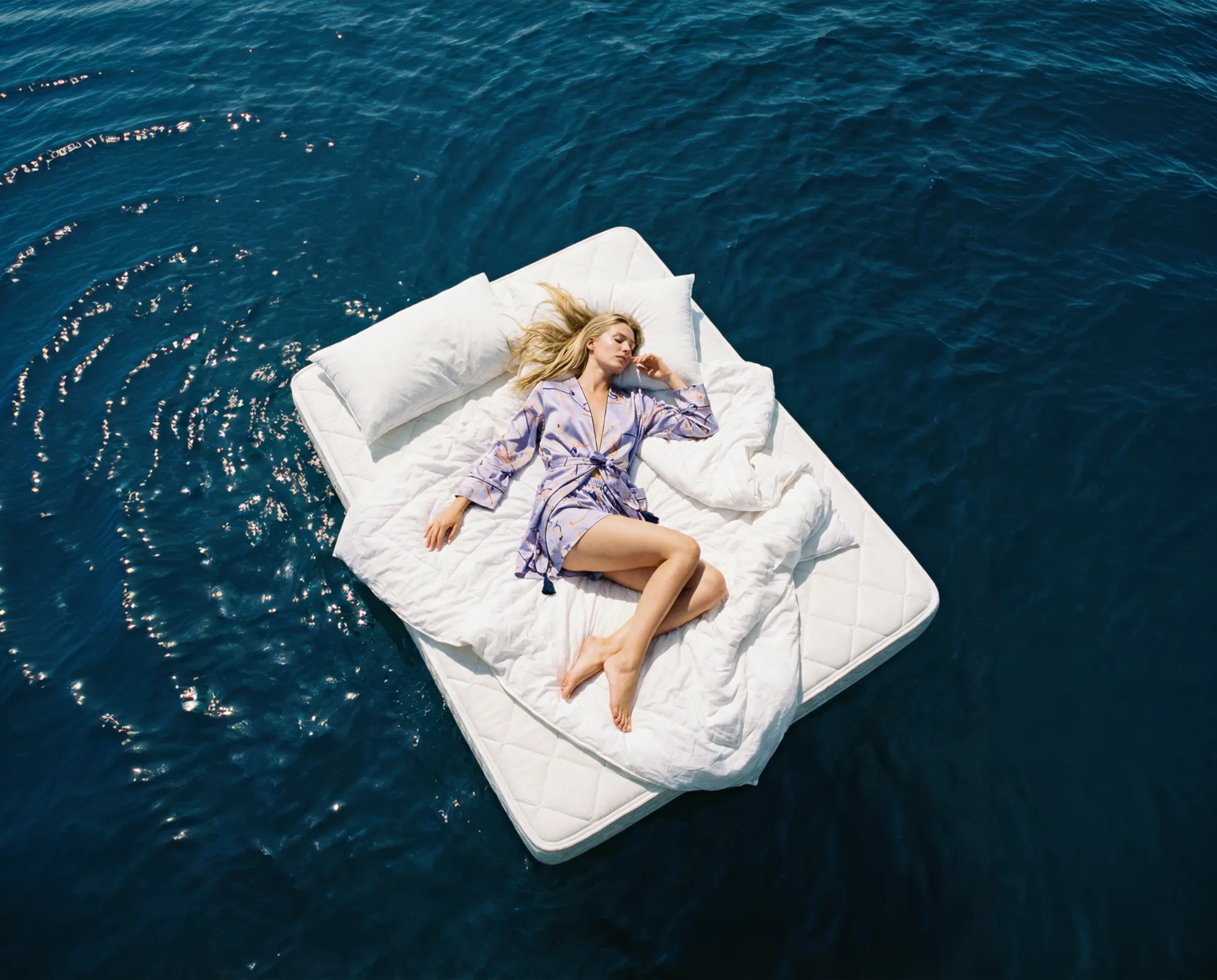 Donna sdraiata su un materasso che galleggia in mare aperto vista dall’alto.