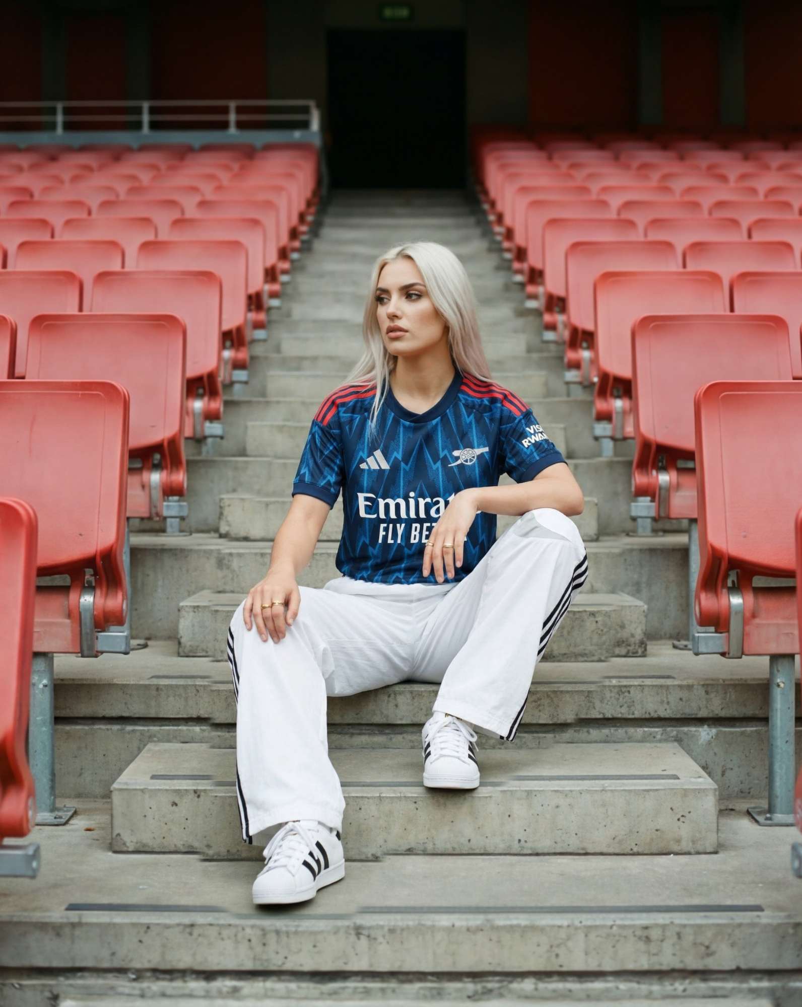 Modella seduta sugli spalti di uno stadio indossando una maglia da calcio blu dell’Arsenal.