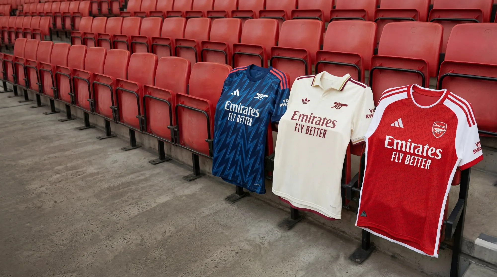 Tre maglie da calcio dell’Arsenal appoggiate sulle sedute rosse dello stadio, fotografia sportiva ambientata sugli spalti.