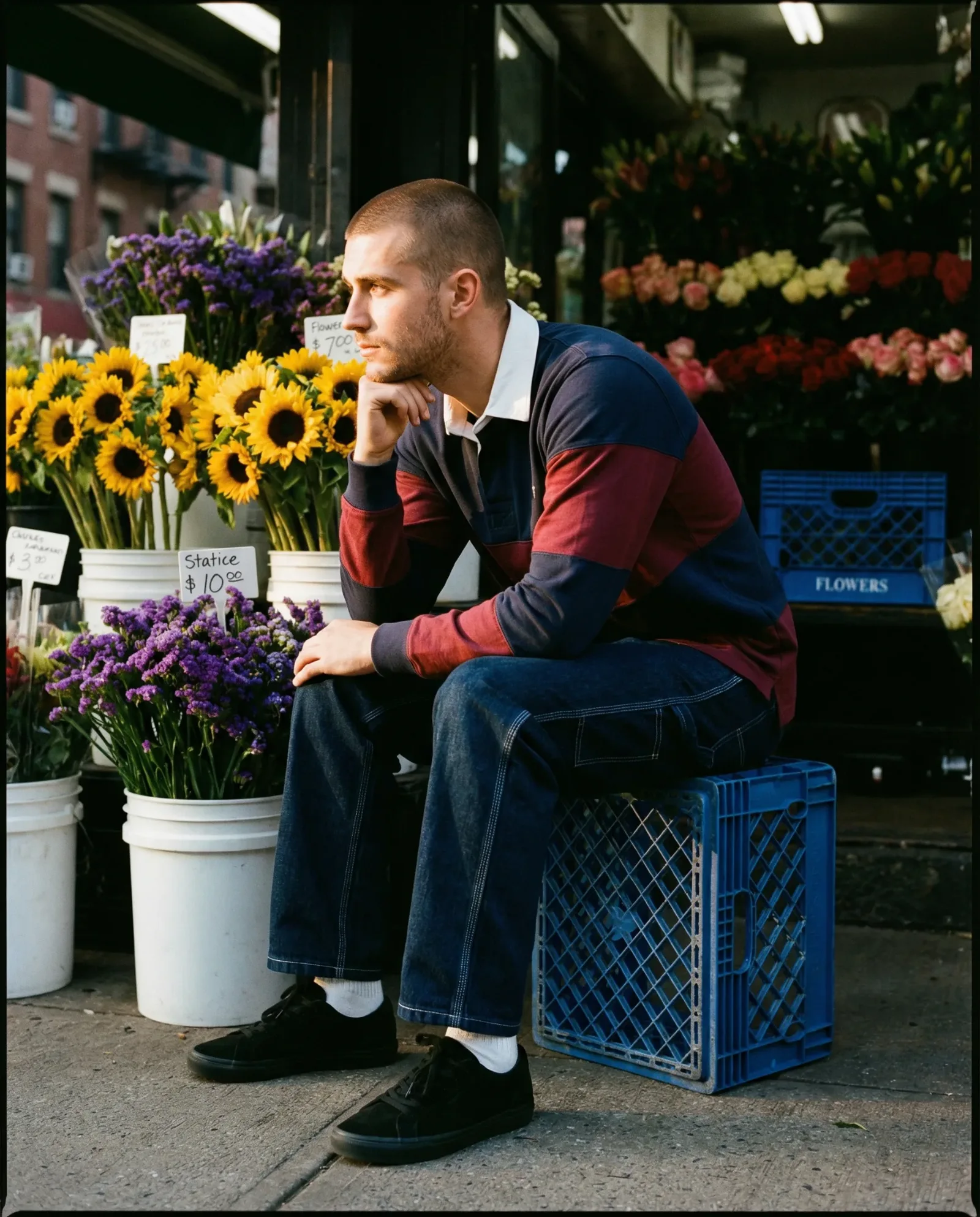 Uomo seduto davanti a un negozio di fiori circondato da girasoli e composizioni floreali.