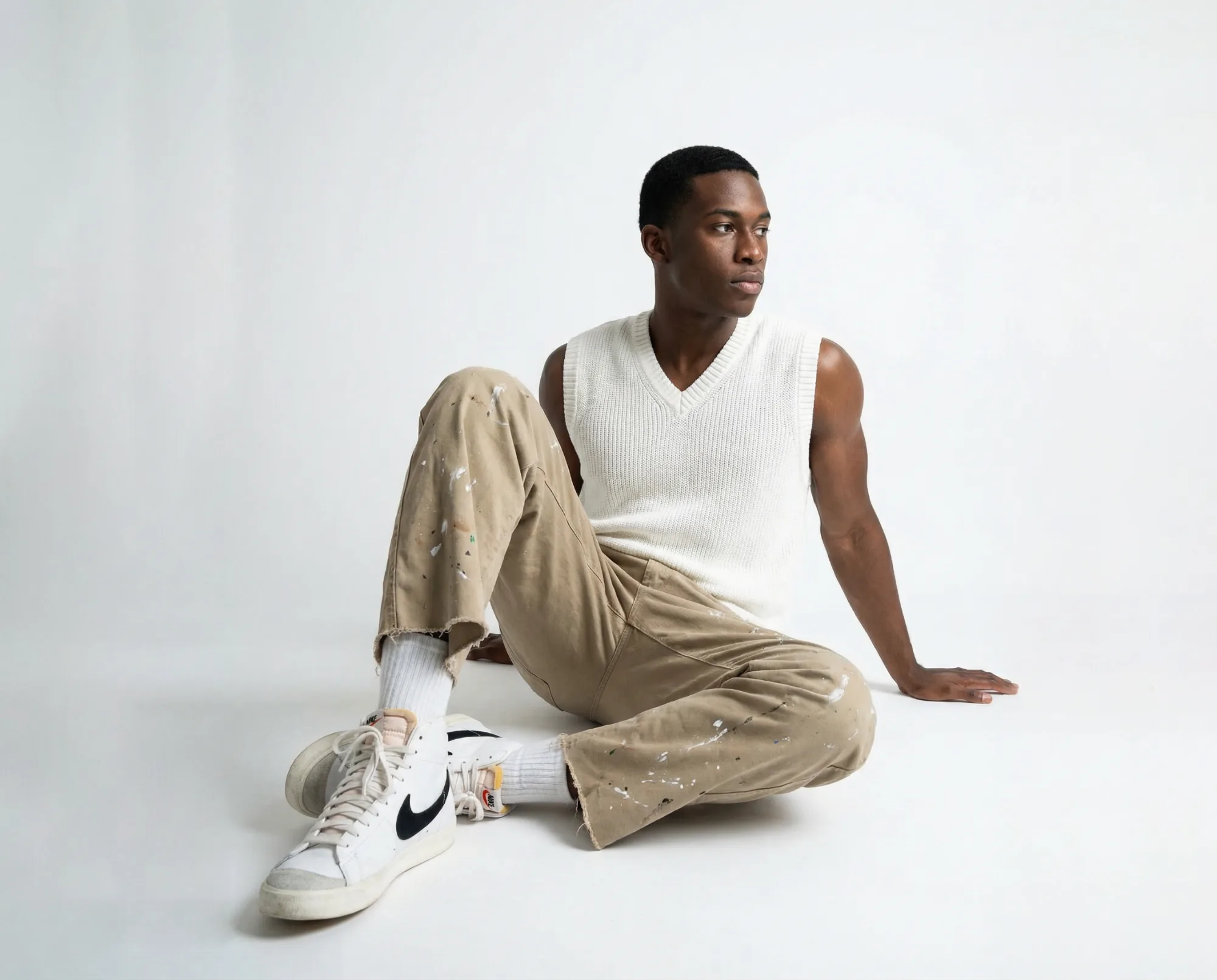 Immagine e-commerce con modello seduto in canotta bianca e pantaloni beige su sfondo neutro