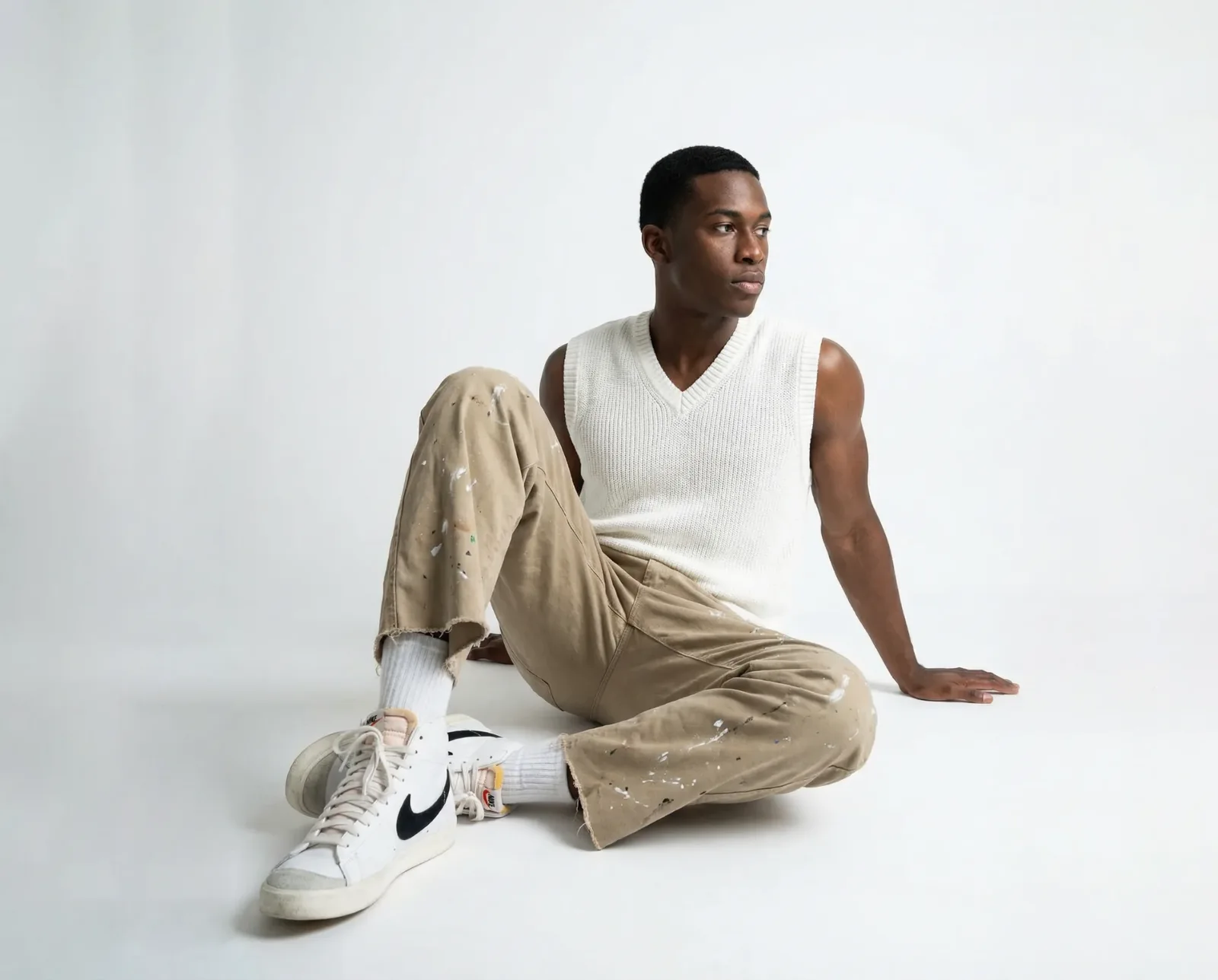 Immagine e-commerce con modello seduto in canotta bianca e pantaloni beige su sfondo neutro