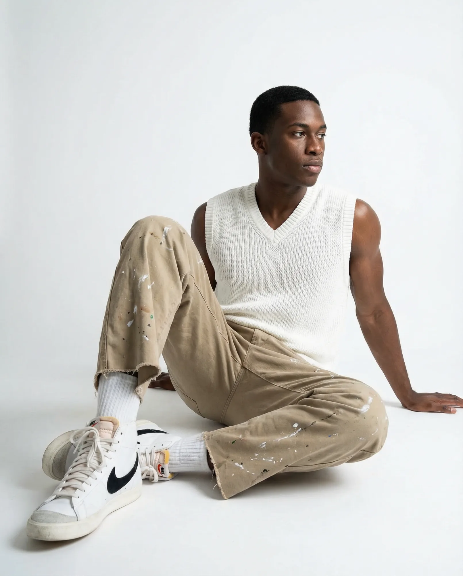 Immagine e-commerce con modello seduto in canotta bianca e pantaloni beige su sfondo neutro
