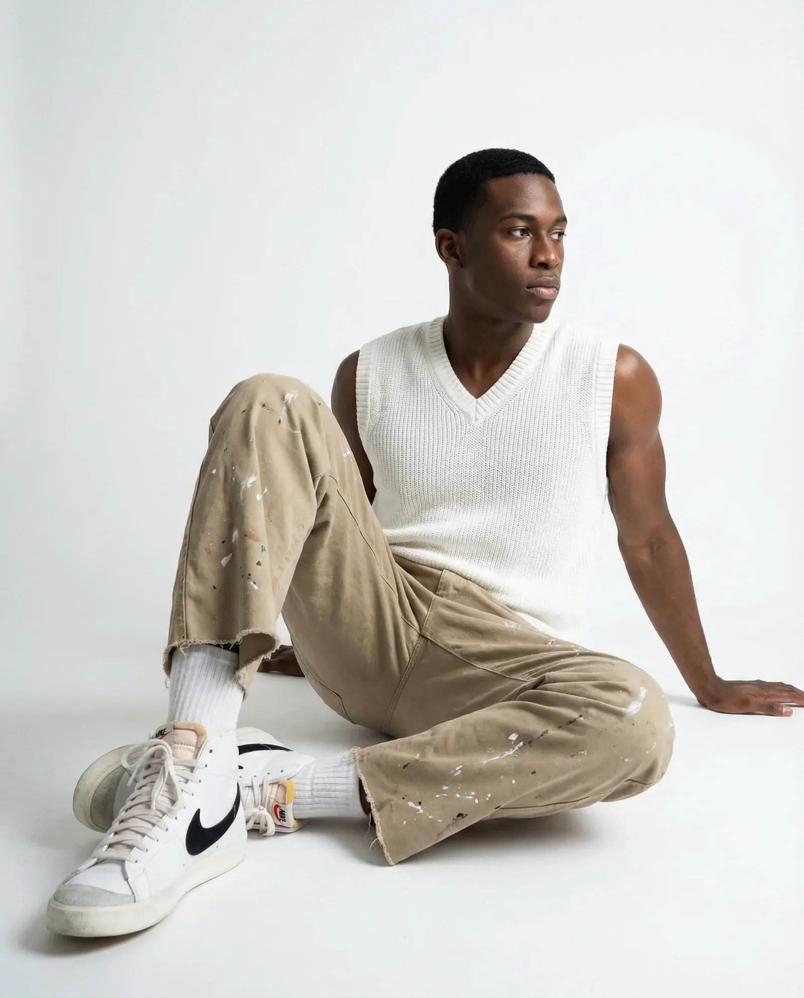Immagine e-commerce con modello seduto in canotta bianca e pantaloni beige su sfondo neutro