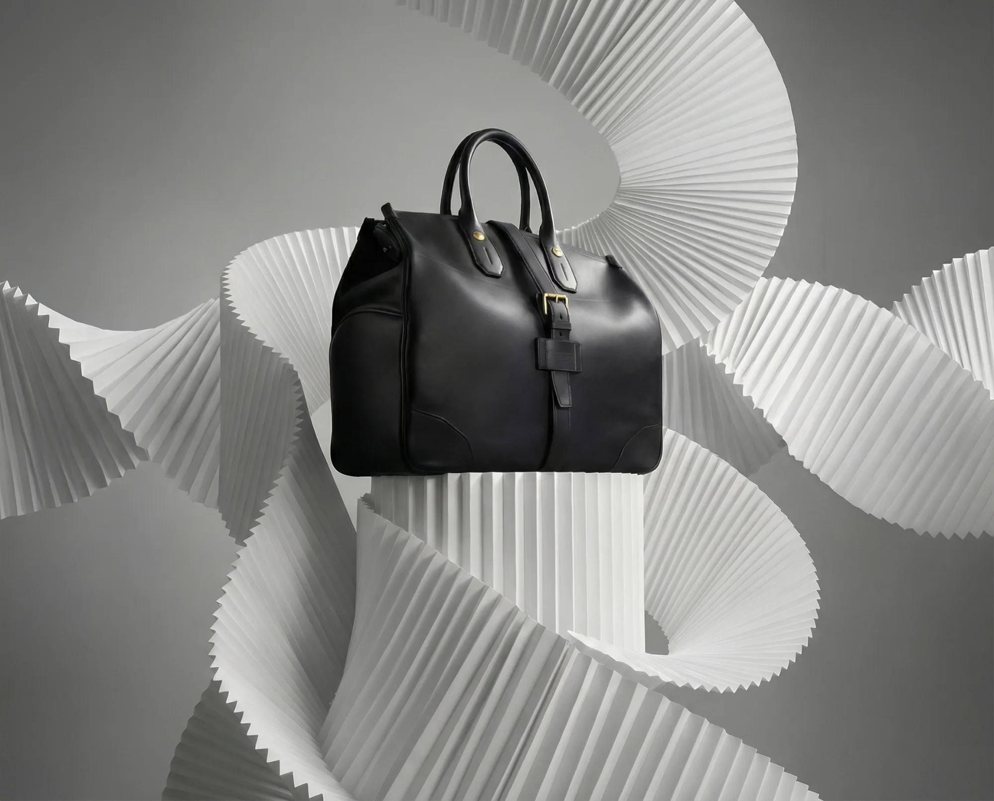 Borsa in pelle nera su piedistallo con sfondo scultoreo bianco ondulato.