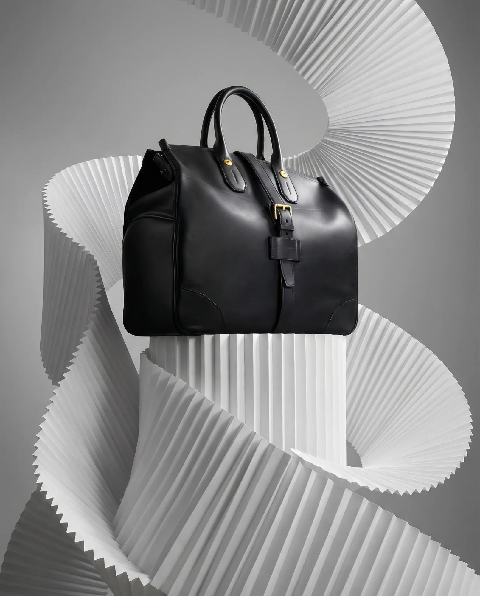 Borsa in pelle nera su piedistallo con sfondo scultoreo bianco ondulato.