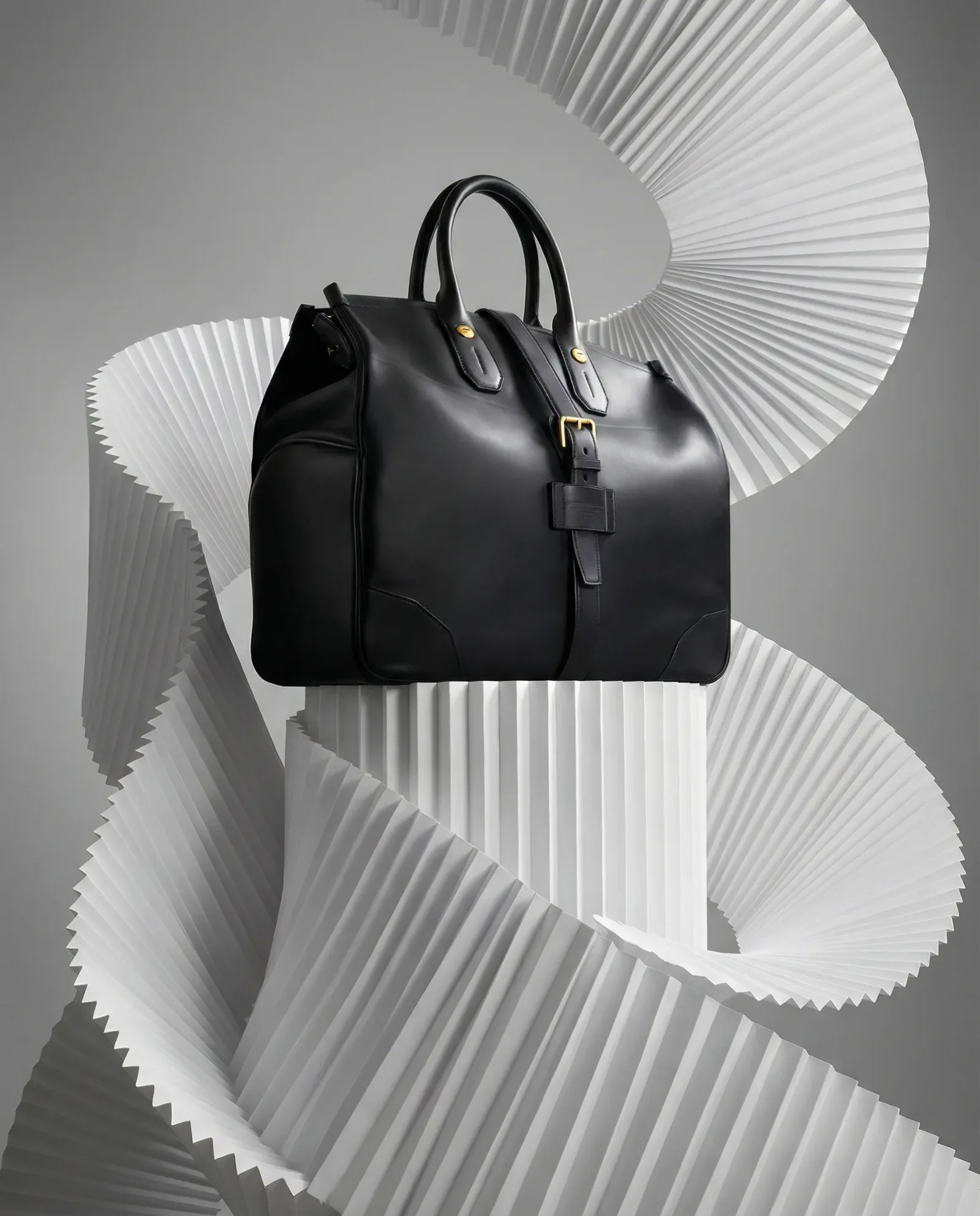 Borsa in pelle nera su piedistallo con sfondo scultoreo bianco ondulato.