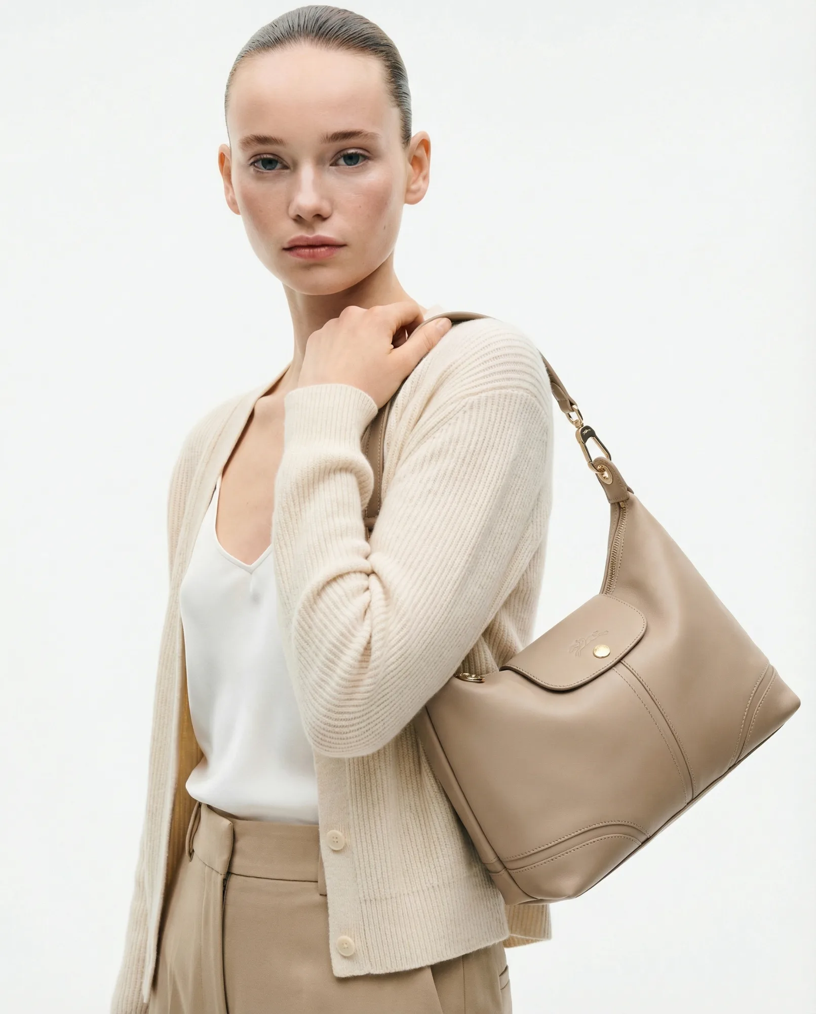 Modella con borsa a spalla beige in pelle, look minimal ed elegante su sfondo neutro