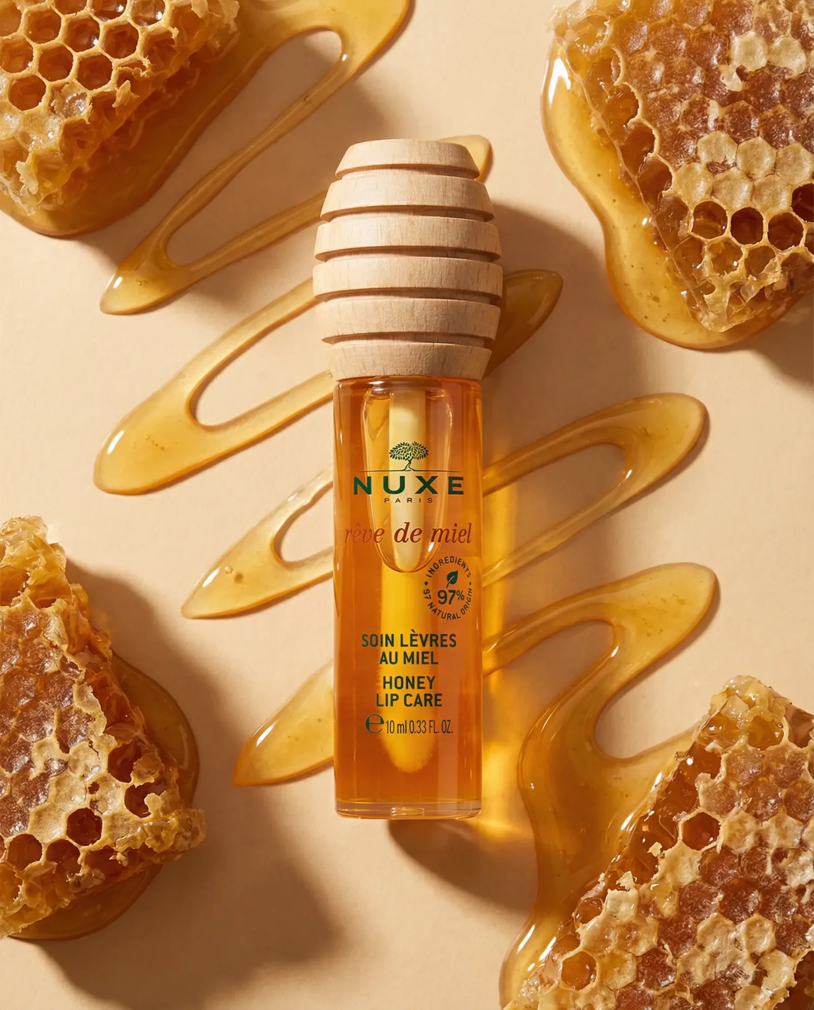 Olio labbra al miele ambientato con colature di miele e favi su fondo beige, fotografia prodotto beauty lifestyle