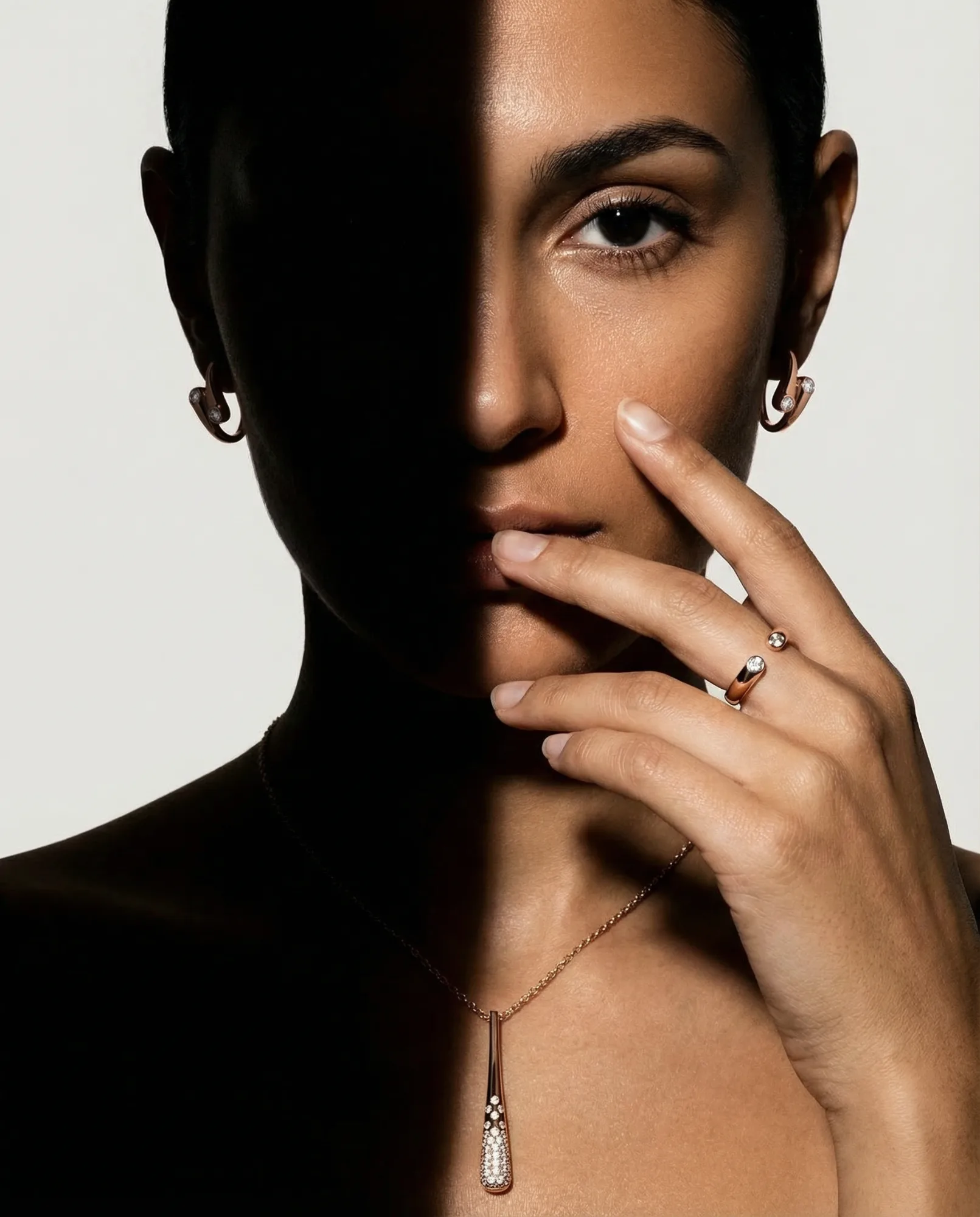 Ritratto femminile con orecchini, anello e collana illuminati da luce drammatica a contrasto, fotografia gioielli editoriale