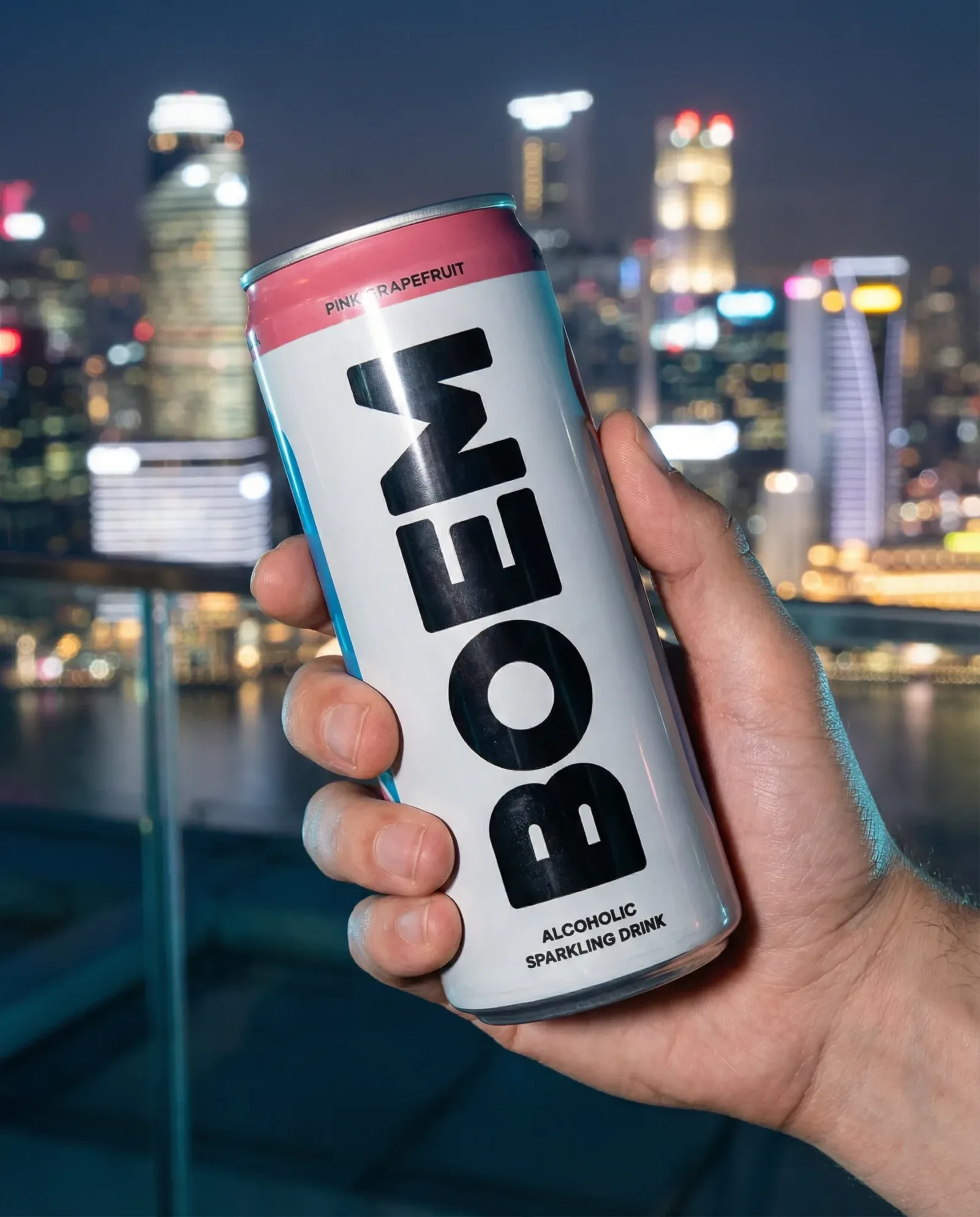 Lattina di bevanda tenuta in mano con skyline urbana illuminata sullo sfondo notturno.