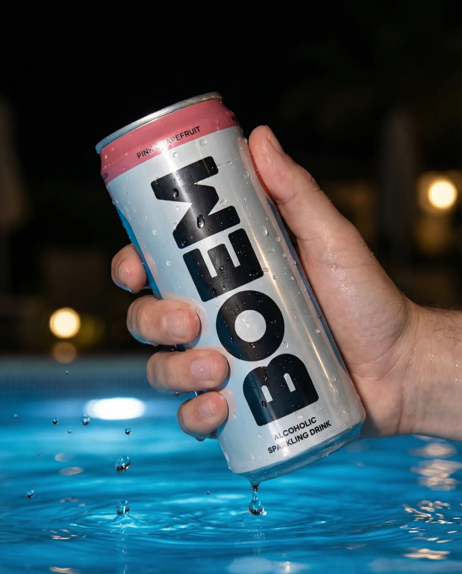 Lattina di bevanda energetica tenuta sopra una piscina illuminata di notte con gocce d’acqua