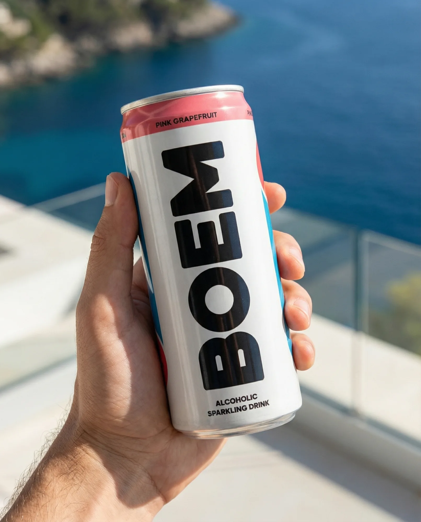 Mano che tiene una lattina slim bianca davanti a una terrazza con vista sul mare blu.