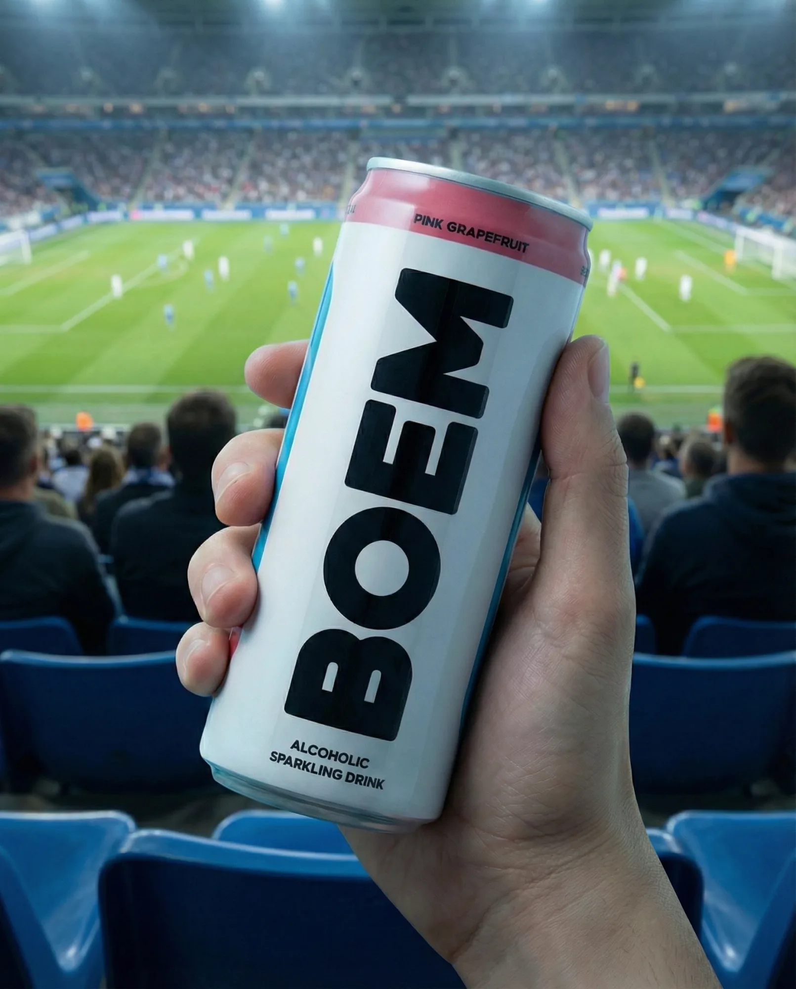 Mano che tiene una lattina di bevanda in uno stadio durante una partita di calcio, con il campo illuminato sullo sfondo.