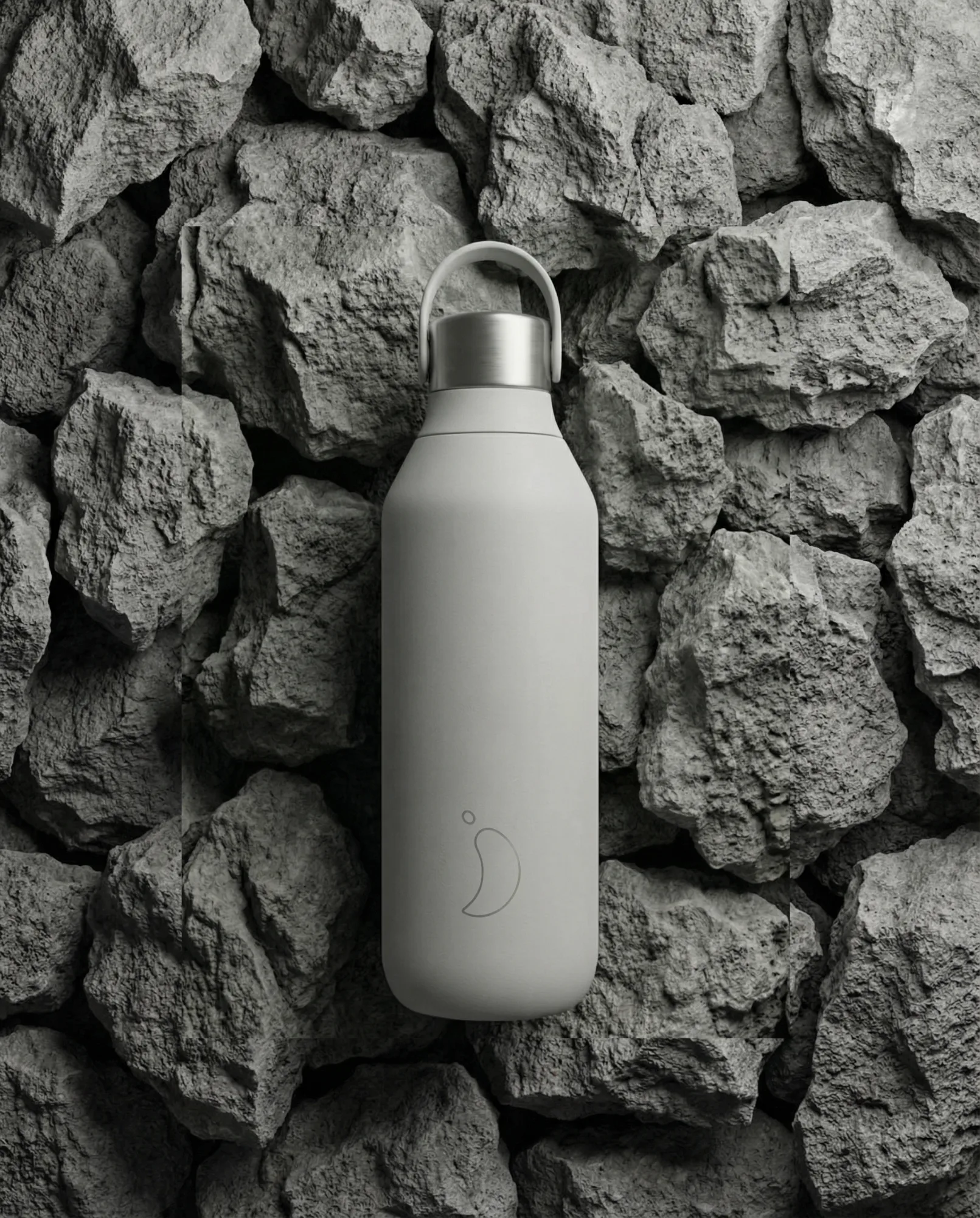 Borraccia termica minimal grigio opaco fotografata su sfondo di rocce vulcaniche, immagine prodotto dal look outdoor moderno