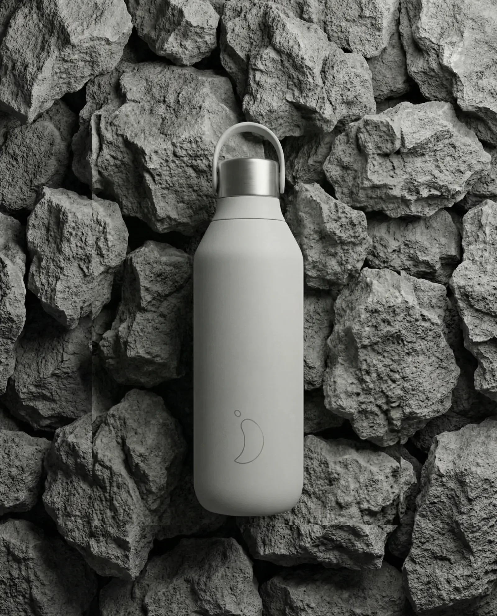 Borraccia termica minimal grigio opaco fotografata su sfondo di rocce vulcaniche, immagine prodotto dal look outdoor moderno