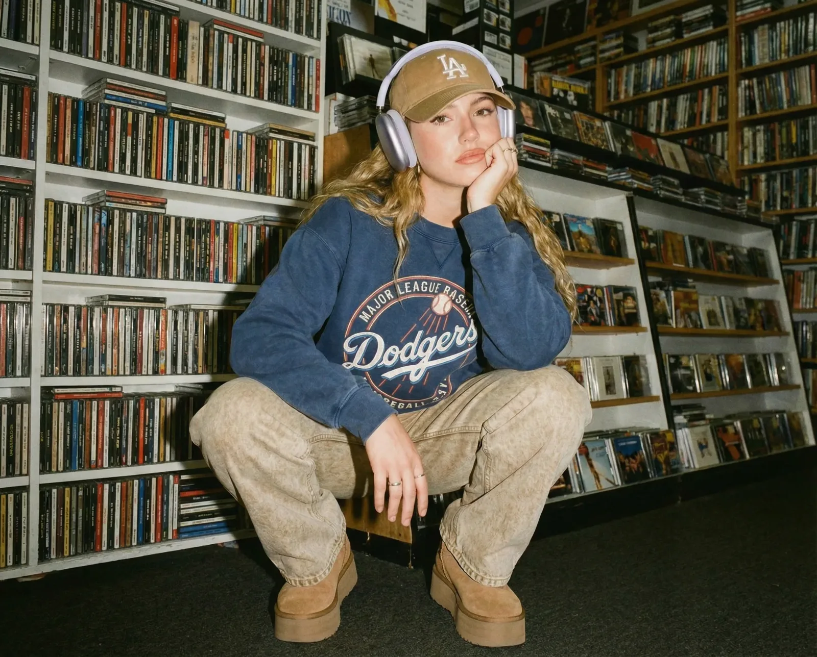 Ragazza seduta davanti a scaffali pieni di CD mentre indossa cuffie over-ear.
