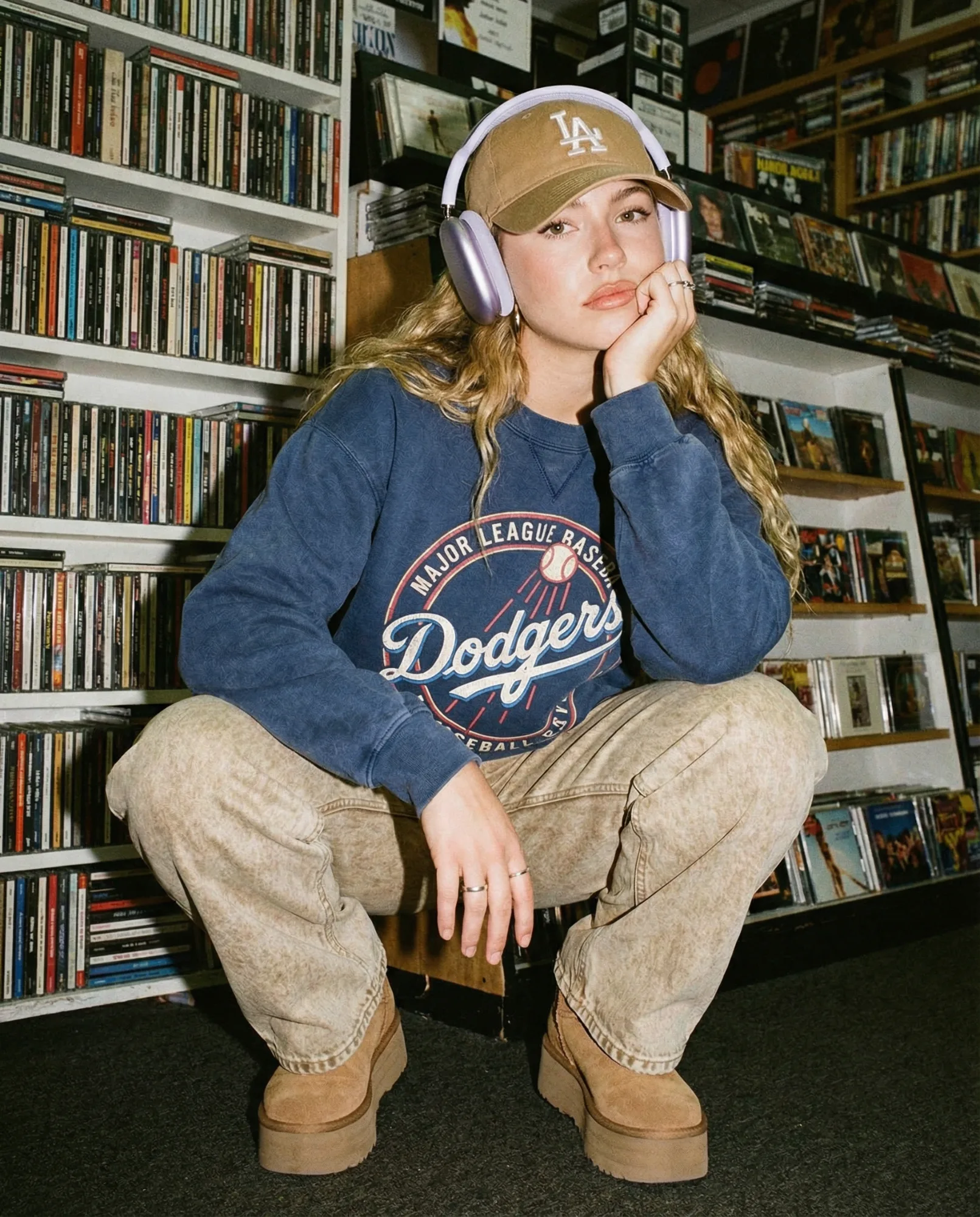 Ragazza seduta davanti a scaffali pieni di CD mentre indossa cuffie over-ear.