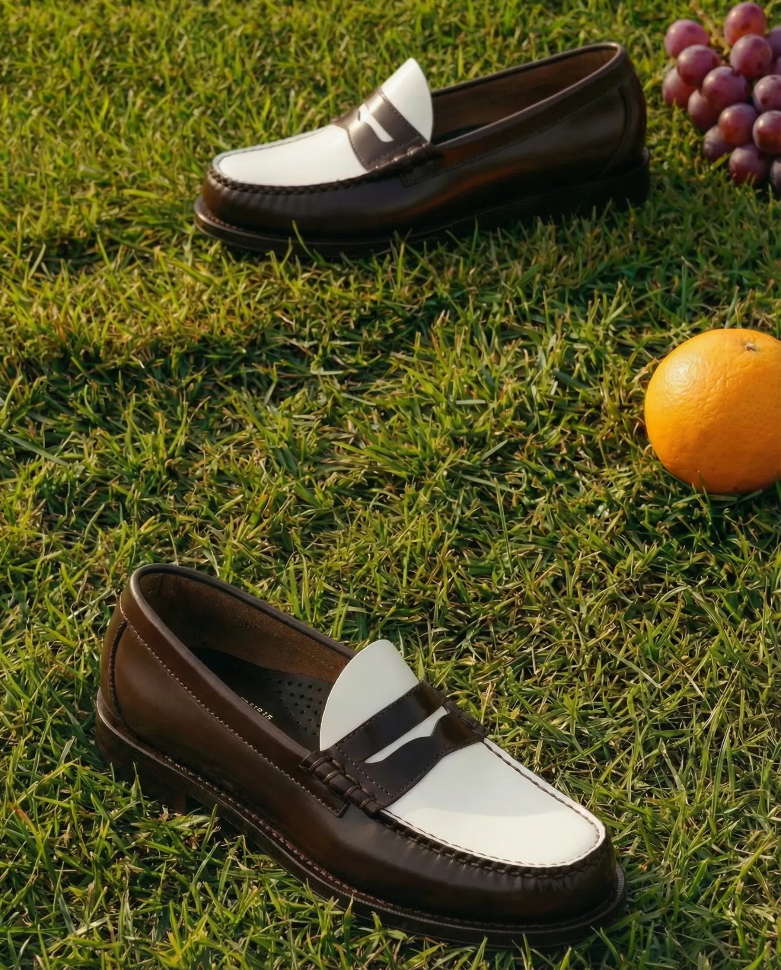 Mocassini in pelle bicolore fotografati su prato verde con arancia e uva, immagine prodotto lifestyle outdoor
