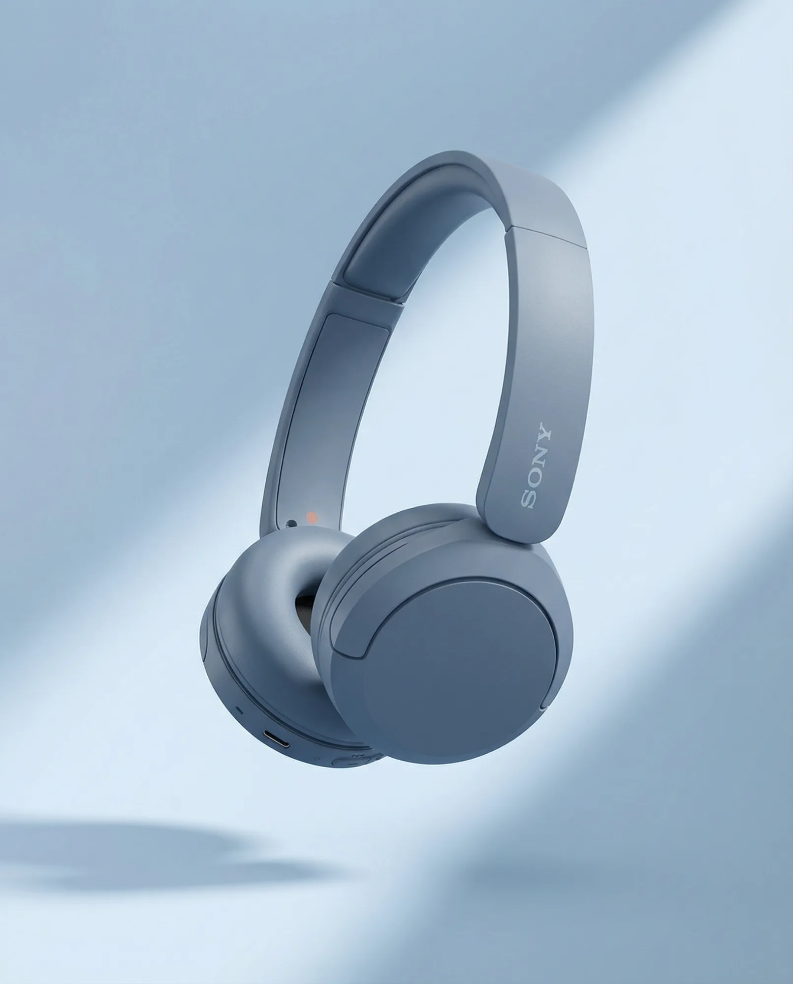 Cuffie wireless over-ear grigie fotografate in sospensione su sfondo blu con luce morbida, immagine prodotto tech minimal