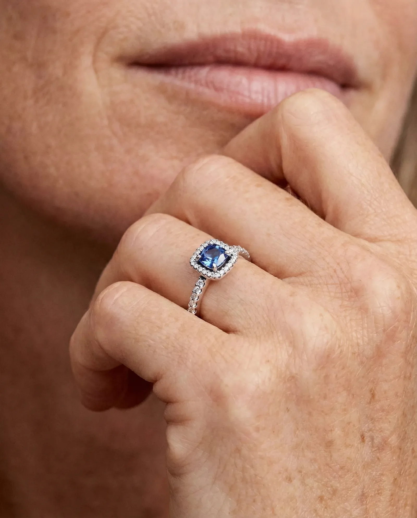 Primo piano di mano con anello in oro bianco e pietra blu circondata da diamanti, fotografia gioiello luxury