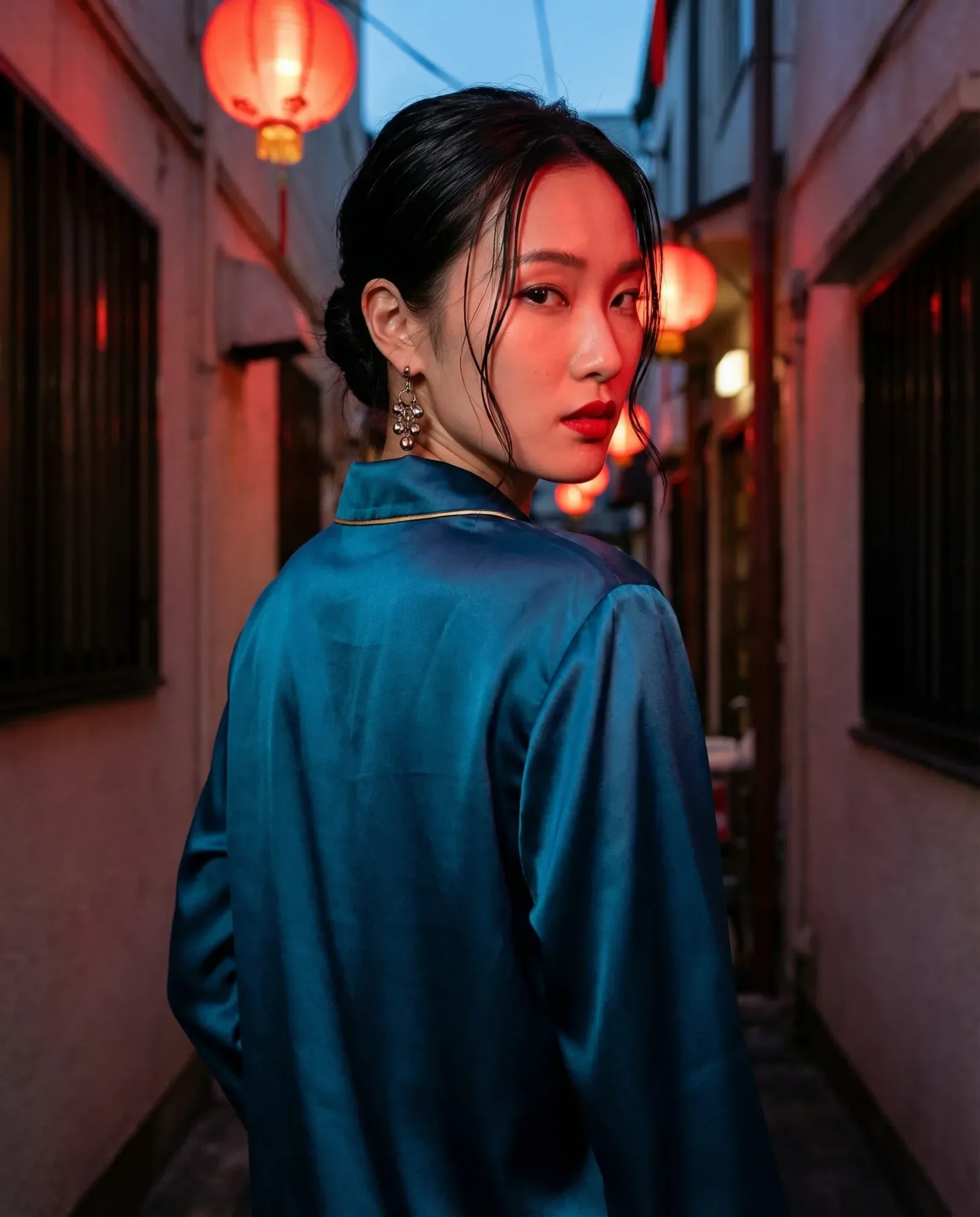 Donna asiatica con camicia satinata blu petrolio che guarda indietro in un vicolo illuminato da lanterne rosse, atmosfera cinematografica notturna con luce calda e ambientazione urbana asiatica.